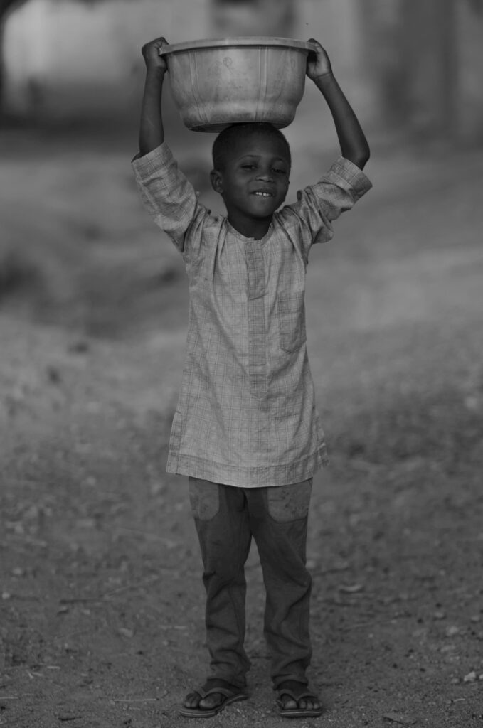 A young boy carrying a water bucket on his head